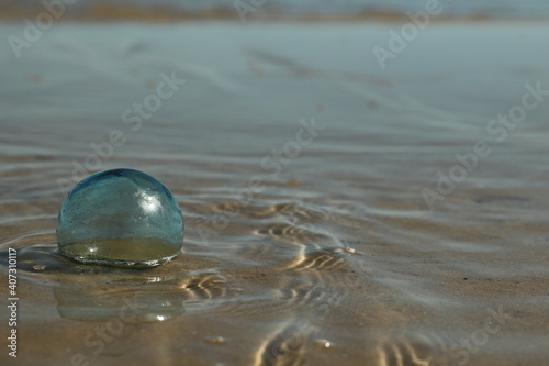 Glass float for a fishing net on the beach caught in the tide; ripples in the water

