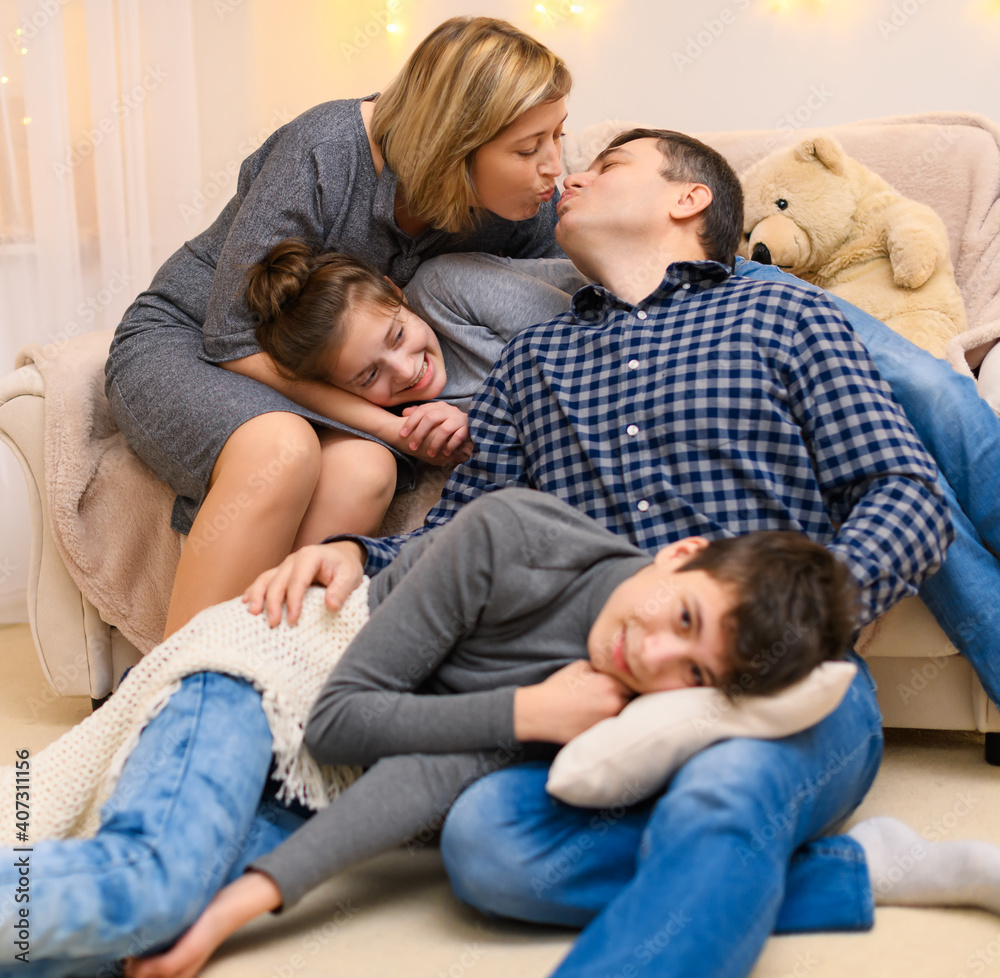 portrait of a family sitting on a sofa at home, four people having fun together, parents kiss