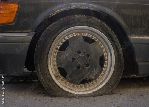 A Black old car, flat tire with black rusty alloy frond wheel. 