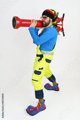 The clown firefighter holds a fire pump in his hands like a grenade launcher.