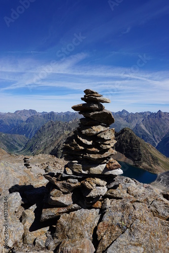Nahaufnahme eines Steinmännchens, im Hintergrund ein Gipfelpanorama