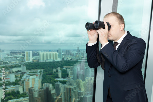 Businessman looks through binoculars from the office window