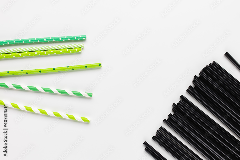 Many black plastic and green eco friendly paper straws on white background. Recycle, environment conversation, pollution and plastic straw ban concept. Copy space