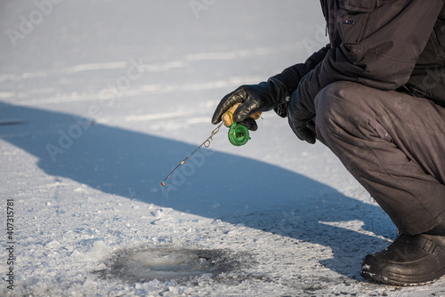 Ice fishing on lake on sunny frosty day. Man sitting near ice hole catching fish. Winter activity.