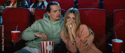 Focused young couple looking emotional while watching movie together, sitting in cinema auditorium