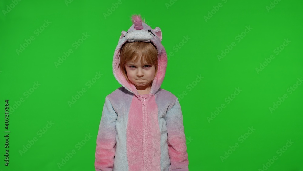 Young little blonde upset child 5-6 years old making faces in unicorn costume on chroma key green background. Portrait of kid girl animator in unicorn pajamas. Copy space Young little blonde upset child 5-6 years old making faces in unicorn costume on chroma key green background. Portrait of kid girl animator in unicorn pajamas. Copy space