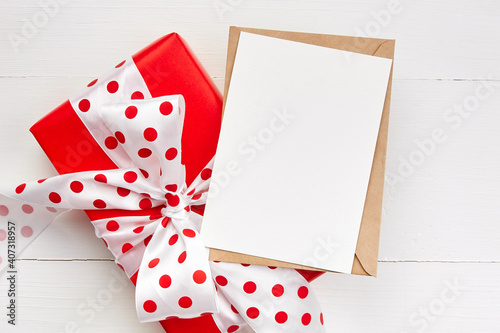 Greeting card mockup and red gift box with big bow on white wooden background