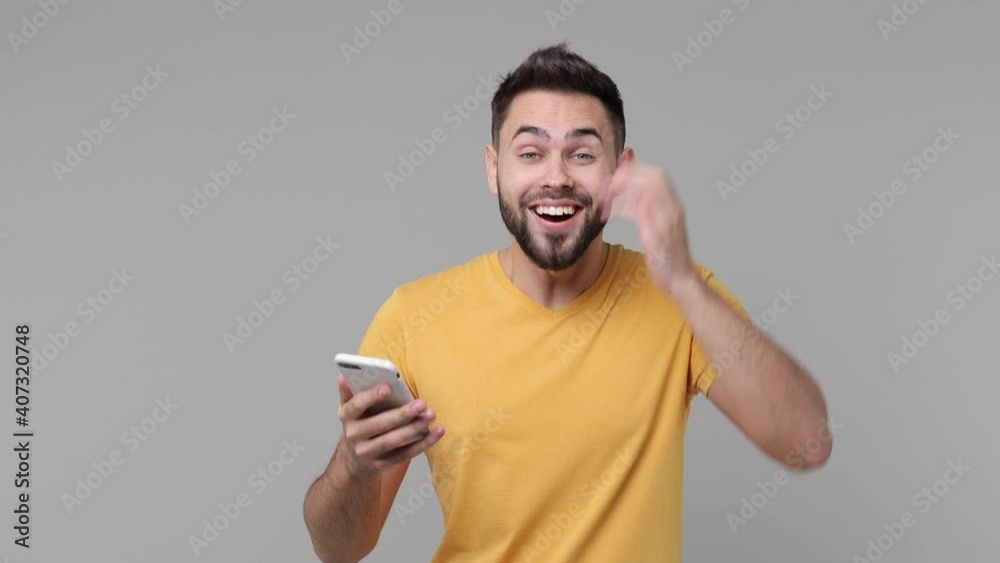 Surprised bearded young man 20s in yellow basic t-shirt isolated on grey background studio. People lifestyle concept. Pointing index finger on mobile cell phone put hand on head doing winner gesture Surprised bearded young man 20s in yellow basic t-shirt isolated on grey background studio. People lifestyle concept. Pointing index finger on mobile cell phone put hand on head doing winner gesture
