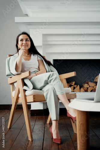 smart businesswoman working sitting on a chair and smiling. Stylish office, dressed in a business suit and shoes. stylish interior background fireplace