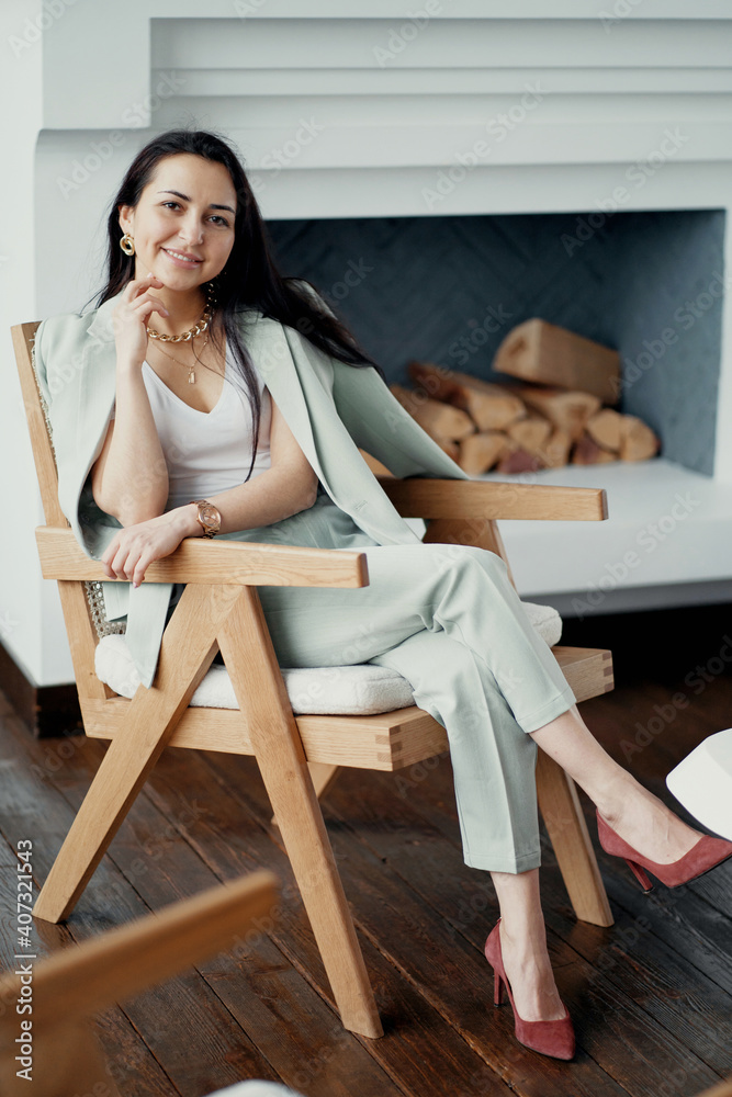 break a bank manager of European appearance is resting sitting on a chair and smiling. Stylish office, dressed in a mint-colored business suit and shoes. background fireplace break a bank manager of European appearance is resting sitting on a chair and smiling. Stylish office, dressed in a mint-colored business suit and shoes. background fireplace