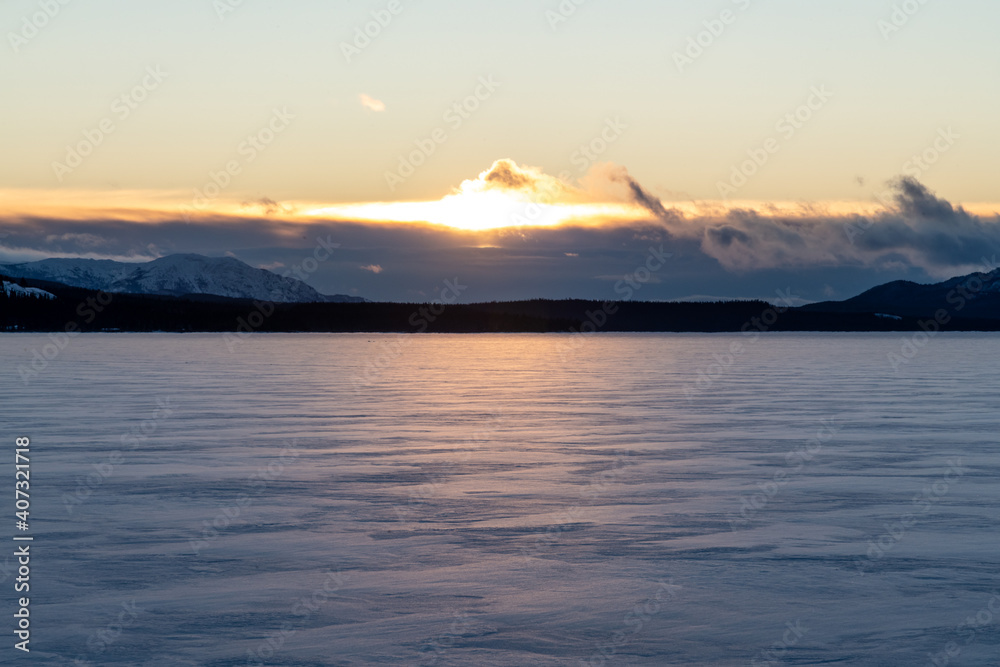 Winter view on a frozen lake in northern Canada, Yukon Territory. Taken in December at sunrise with clouds in the distance. Snow covered body of water below. 