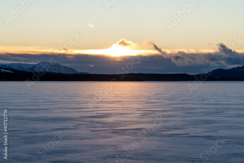 Winter view on a frozen lake in northern Canada  Yukon Territory. Taken in December at sunrise with clouds in the distance. Snow covered body of water below. 