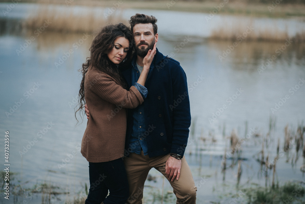 two caucasian lovers near the lake. Young couple is hugging on autumn day outdoors. A bearded man and curly woman in love. Valentine's Day. Concept of love and family