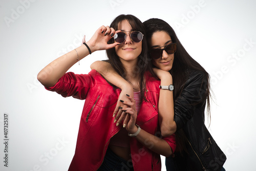 Twin sisters hugging. Teen twins wearing leather jackets and sunglasses on light background