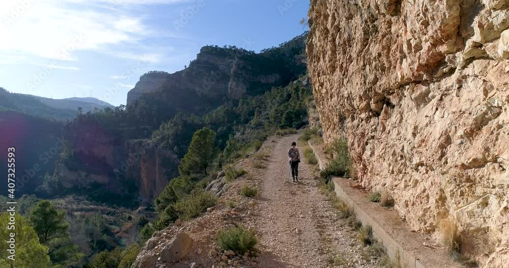 dron vuela hacia atrás adolescente con bastón camina en senda junto a barranco montañoso