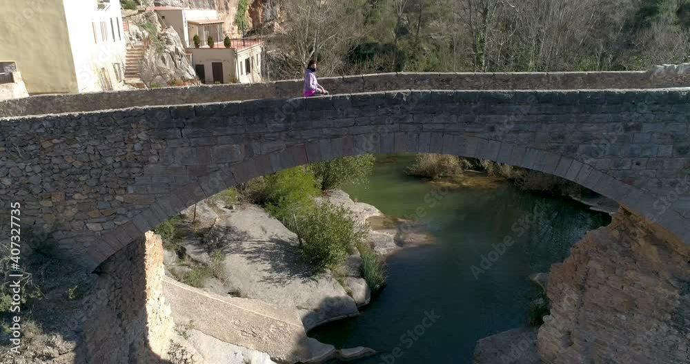Mujer con mascarilla covid-19 sentada en alto puente medieval dron volando hacia abajo