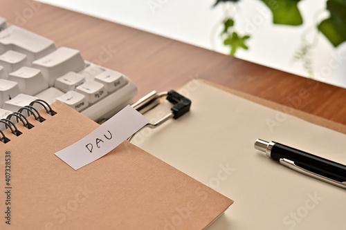 A sticky note labeled DAU is taped to the edge of a notebook on the desk.That s an acronym for Daily Active Users.