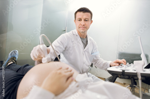Close up portrait of man doctor using ultrasound to check fetal health of his patient, young pregnant woman. Medical and healthcare concept. Obstetrics, gynecology and ultrasound