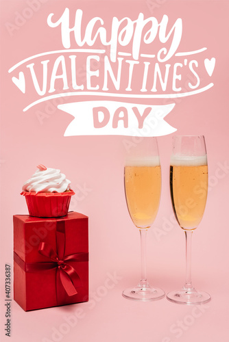champagne glasses near gift  cupcake and happy valentines day lettering on pink