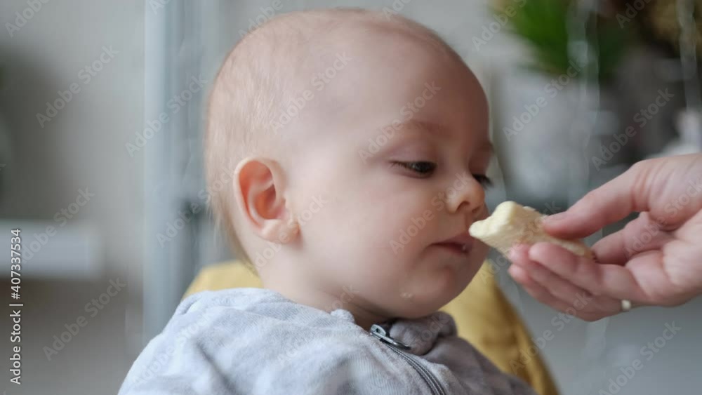 Mother's hand feeding baby. Little 9 month old baby boy eating banana in the kitchen. Mother's hand feeding baby. Little 9 month old baby boy eating banana in the kitchen.
