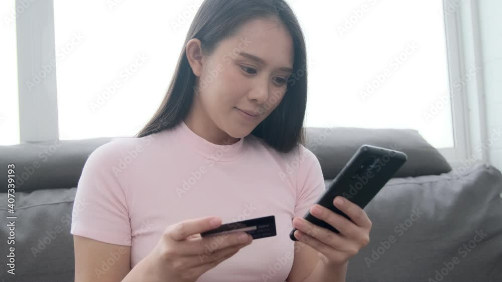 Online payment of Asian woman using credit card and smart mobile phone to pay digital currency money cash transaction from purchasing ecommerce products, happy smiling relaxing home living room. Online payment of Asian woman using credit card and smart mobile phone to pay digital currency money cash transaction from purchasing ecommerce products, happy smiling relaxing home living room.