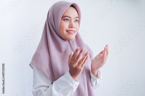 Asian Islam Muslim woman in headscarf and hijab prays with her hands up in air with smile face. Indonesian woman. Religion praying concept isolated on grey background