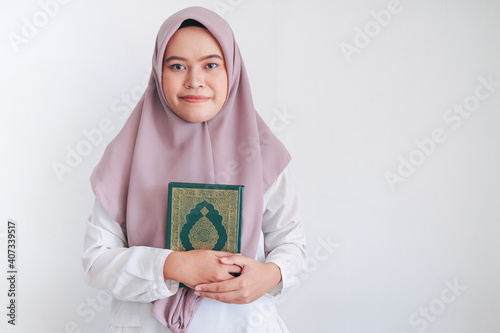 Young Asian Islam woman wearing headscarf is holding holy al quran in hand with smile and happy face. Indonesian woman on gray background photo