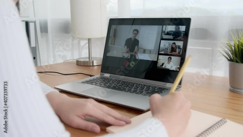 Online team meeting conference happy Asian woman working at home social distancing, using computer laptop video conference call writing on notebook planning marketing strategy for business company.