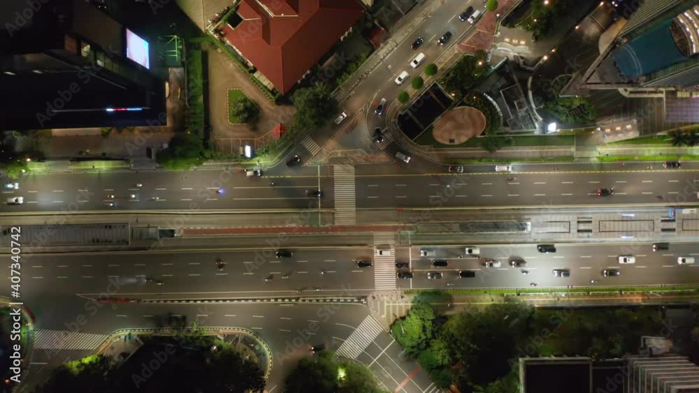 Top down overhead birds eye aerial view of cars and motorcycles driving through a busy multi lane intersection at night in large city in Asia