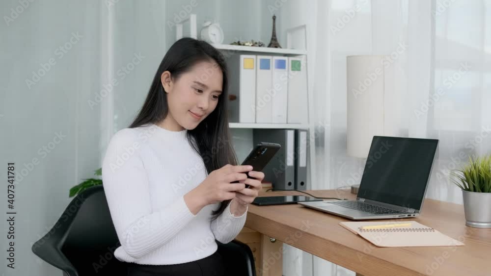 Happy smiling Asian business woman using smart phone mobile device, working at home modern office sitting at desk working business agency with laptop tablet computer device technology quarantine. Happy smiling Asian business woman using smart phone mobile device, working at home modern office sitting at desk working business agency with laptop tablet computer device technology quarantine.