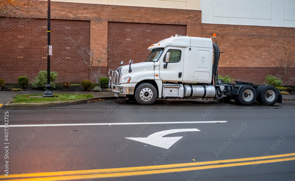 White big rig powerful semi truck with low cabin and grille guard standing on the street parking in industrial zone