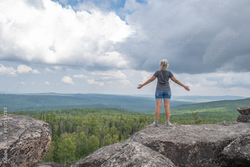 Naklejka premium A happy middle-aged woman stands on the top of a mountain enjoying an amazing view.Active recreation and travel concept.