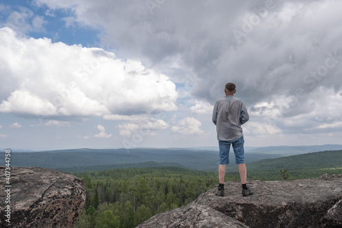 A middle-aged man at the top of the mountain enjoys a stunning view of the hilly valley. Freedom and goal achievement.