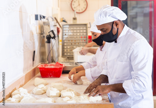 Latin american man working with his wife in family bakery, forming bread loaves from raw dough