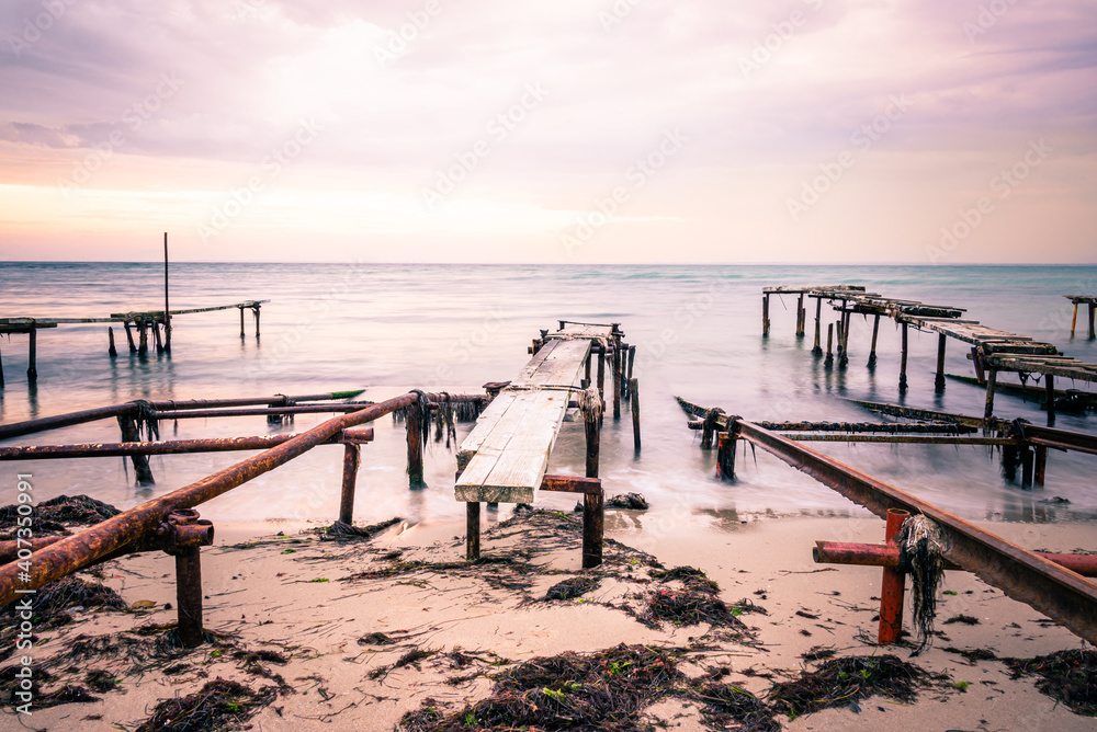 Colorful sunset over the sea shore. Old rusty boat berths. Long exposure smooth water waves effect.
