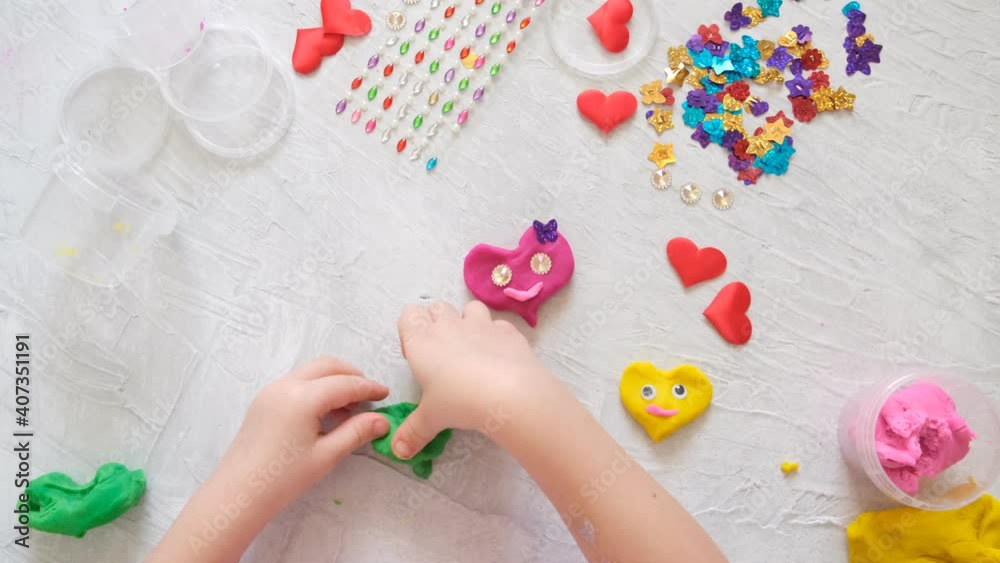 Holiday crafts. Child playing with colorful modeling clay sculpting heart figure with beads and sequins . Home Education game with clay. Early development concept Holiday crafts. Child playing with colorful modeling clay sculpting heart figure with beads and sequins . Home Education game with clay. Early development concept