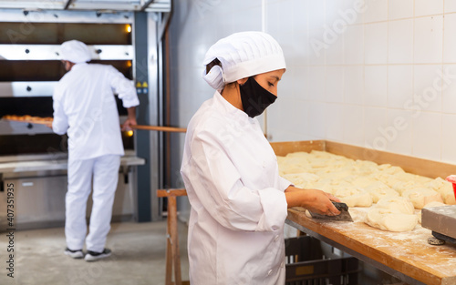 Young latin american woman working in bakery, preparing portioned pieces of dough for baking