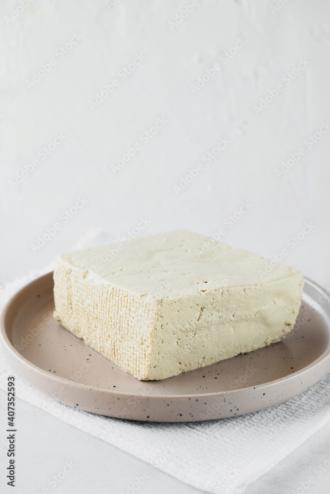 tofu cheese is large piece on plate on white background. Healthy dietary vegetarian food, vertical food content, selective focus