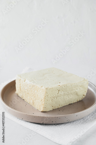 tofu cheese is large piece on plate on white background. Healthy dietary vegetarian food, vertical food content, selective focus