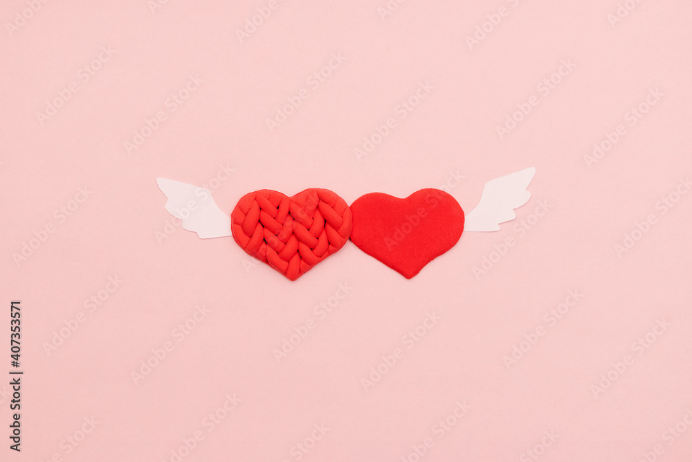 Two red textured hearts with white angel wings on a pink background.Valentine's day background.Flat lay, top view.