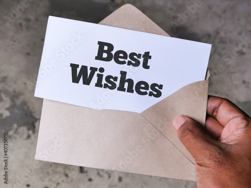 Selective focus image with noise effect hand holding envelope with white card written text BEST WISHES.