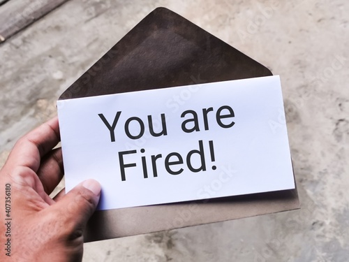 Selective focus image with noise effect hand holding envelope with white card written text YOU ARE FIRED.