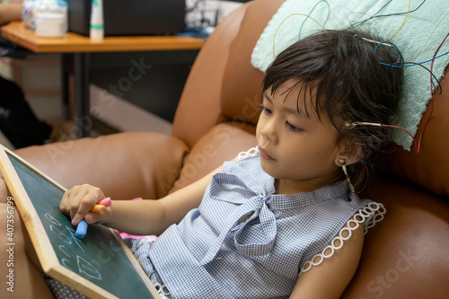 Little girl sitting on chair with EEG electrodes attached to her head.