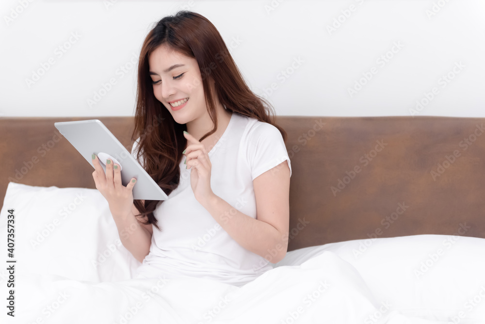 Beautiful asian woman Using the tablet On the bed in the white bedroom Beautiful asian woman Using the tablet On the bed in the white bedroom