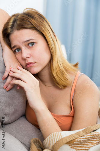 Young sad female sitting on cozy sofa and melancholy at home photo