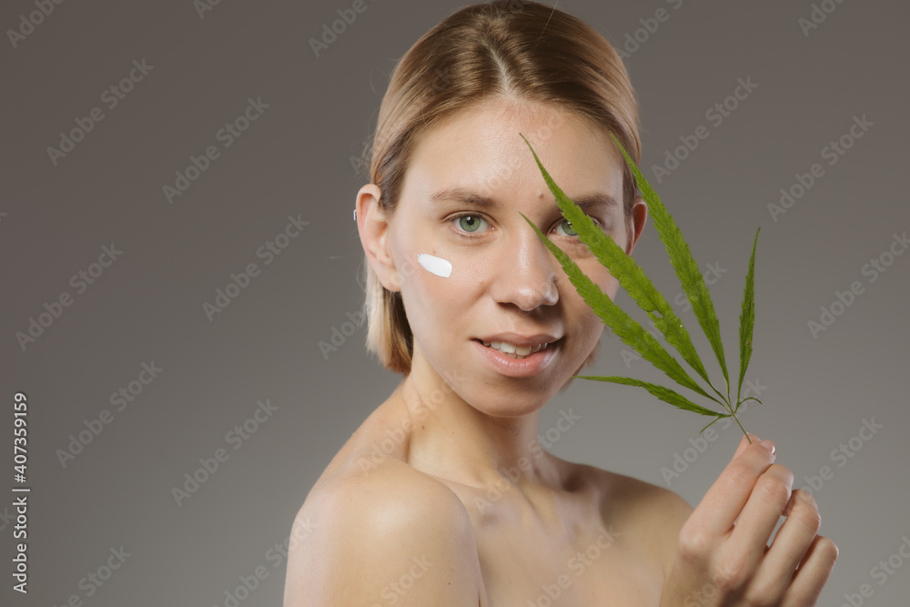 CBD cosmetics concept. Beautiful woman with a cannabis leaf on gray background CBD cosmetics concept. Beautiful woman with a cannabis leaf on gray background
