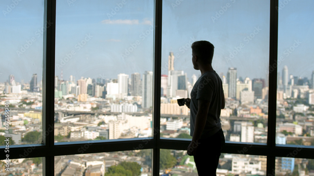 Dreaming european man stands by the window with great views and drinks hot coffee or tea, enjoying beautiful morning feeling happy Dreaming european man stands by the window with great views and drinks hot coffee or tea, enjoying beautiful morning feeling happy