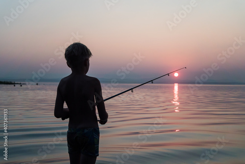 boy fishing with a fishing rod standing in the water in the evening at sunset