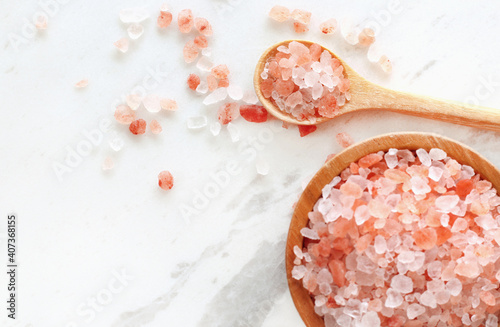 top view of himalayan pink rock salt in wooden bowl and spoon on white marble table. photo