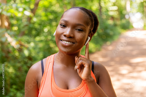 fitness, sport and technology concept - happy smiling young african american woman with wireless earphones listening to music outdoors